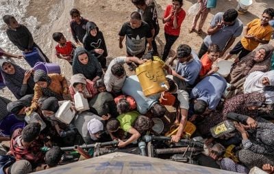 People gather with jerrycans and other containers to collect water from a tanker cistern in Deir el-Balah in the central Gaza Strip