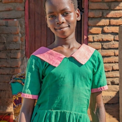 A girl dressed in her school uniform stands in front of her family's home