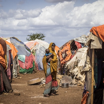 Somalian woman carrying child, surrounded by informal tents 