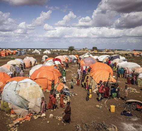 People surrounding orange and white makeshift tents in Somalia IDP camp