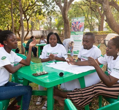 Four Malawian students sit at green table discussing climate change