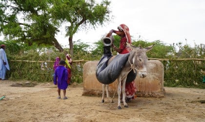 Woman filling water jugs from a well.