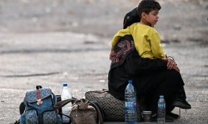 A woman sits with a child on her lap next to bags on the ground as people fleeing from Lebanon arrive on the Syrian side of the border with Lebanon in Jdeidat Yabus in southwestern Syria on September 24, 2024. (Photo: Louai Beshara/AFP via Getty Images)