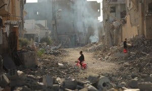 Child on tricycle cycles through destroyed buildings in Gaza