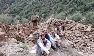 Four men sitting next to a completely collapsed building in Kunar Valley, Afghanistan