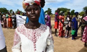Ajok Deng, a woman in South Sudan wears a white dress, holding some cash. Behind her is a queue of people
