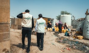 Concern’s health staff and the Country Director Victor Moses visit a displacement camp in Yemen, with people filling a water tank in the background