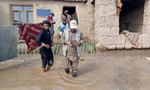 Concern staff member walking through flooded garden of a home with family members behind him