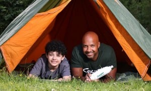 Two people, a man and an older child, in a tent outside looking straight ahead