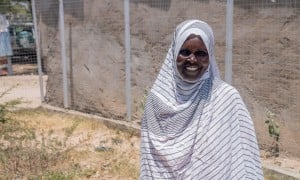 Woman smiling, stand outside wearing a white and grey striped head scarf