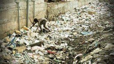 A boy searches through waste in an alleyway.