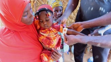 Young girl held by her mother getting her arm measured by doctor