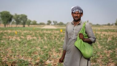 Farmer Maula stands in field in Pakistan with green bag of seeds