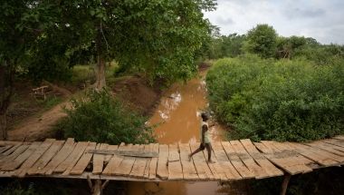 A man uses a small bridge to cross a river in Tana River County, Kenya
