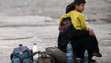 A woman sits with a child on her lap next to bags on the ground as people fleeing from Lebanon arrive on the Syrian side of the border with Lebanon in Jdeidat Yabus in southwestern Syria on September 24, 2024. (Photo: Louai Beshara/AFP via Getty Images)