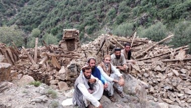 Four men sitting next to a completely collapsed building in Kunar Valley, Afghanistan