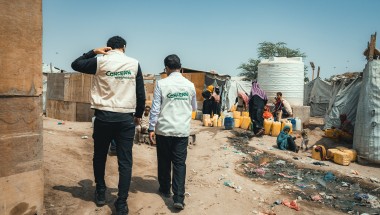 Concern’s health staff and the Country Director Victor Moses visit a displacement camp in Yemen, with people filling a water tank in the background