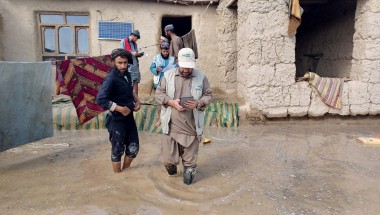 Concern staff member walking through flooded garden of a home with family members behind him