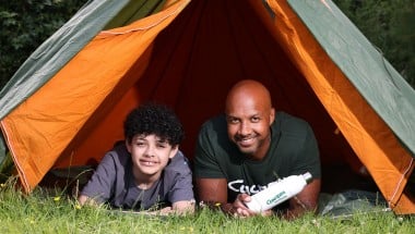Two people, a man and an older child, in a tent outside looking straight ahead