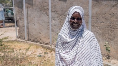 Woman smiling, stand outside wearing a white and grey striped head scarf