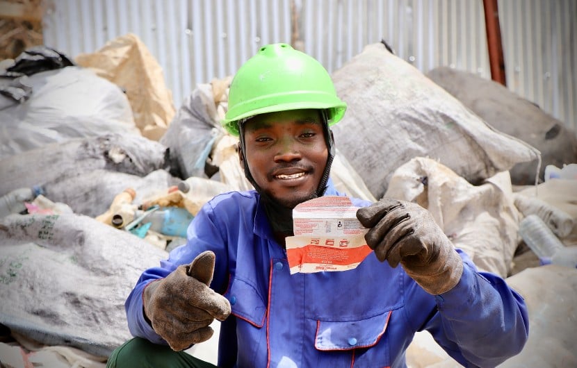 A Karo Enterprise employee holds an empty red and white RUTF sachet, which will be recycled into eco-friendly bricks and paving stones.