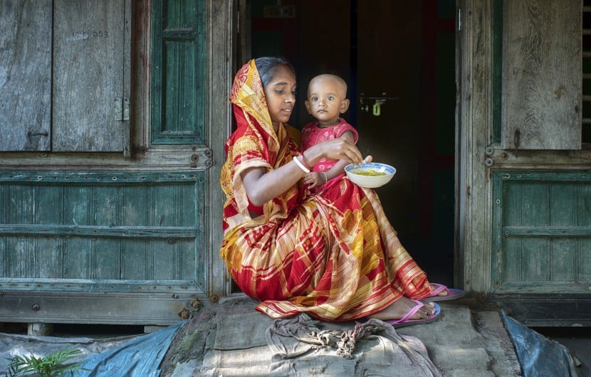 Mitali Mondal is feeding nutritious food to her eighteen months old daughter, Mahi. Every month mothers of the Haldi Bunia community get together once, arrange nutritious meals for their small kids, and feed them together. This session helped mothers to teach each other nutritious meals for their growing children. Several mothers get together and support with the cooking steps. The mother group receives ingredients from the Collective Responsibility, Action, and Accountability for Improved Nutrition (CRAAIN