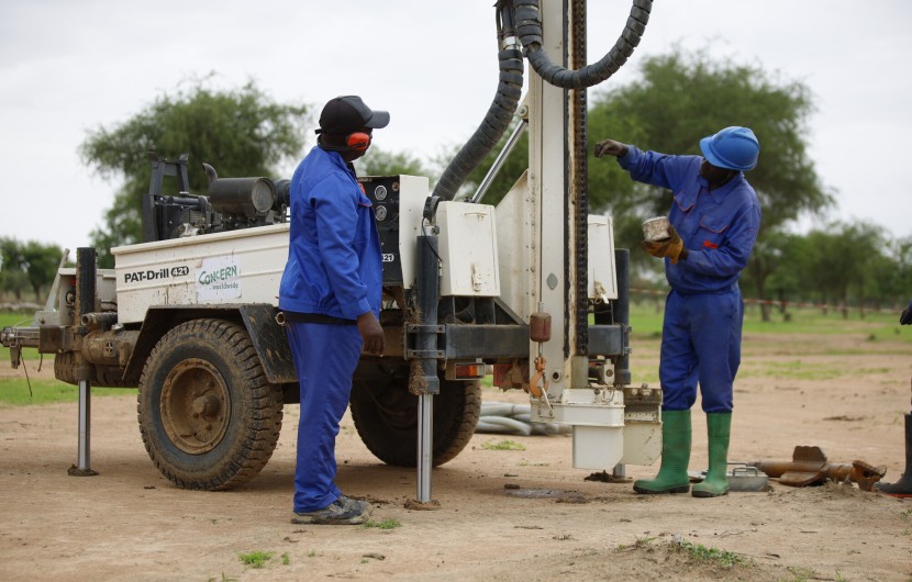 Two men with a machine which is boring a hole into the ground