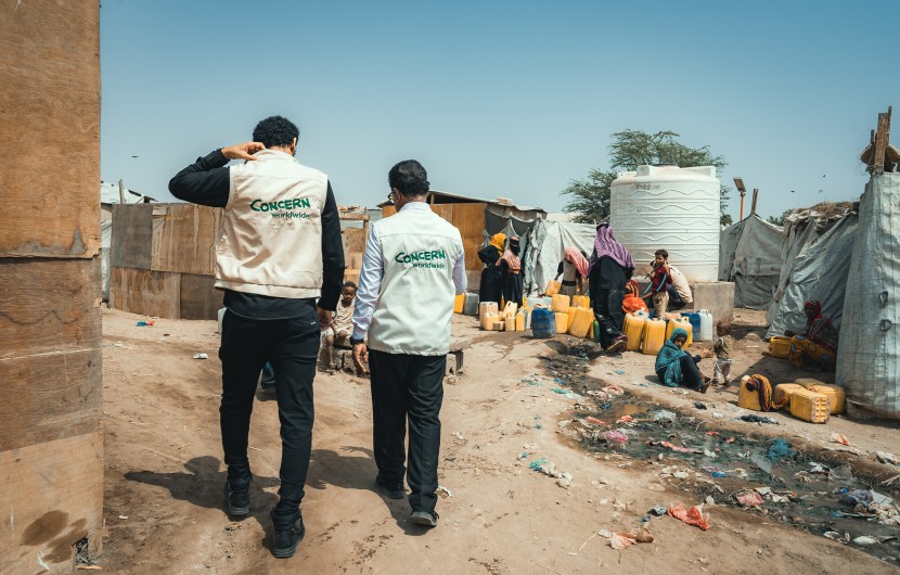 Concern’s health staff and the Country Director Victor Moses visit a displacement camp in Yemen, with people filling a water tank in the background