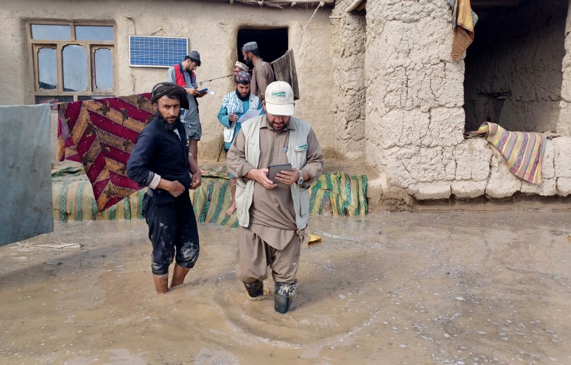 Concern staff member walking through flooded garden of a home with family members behind him