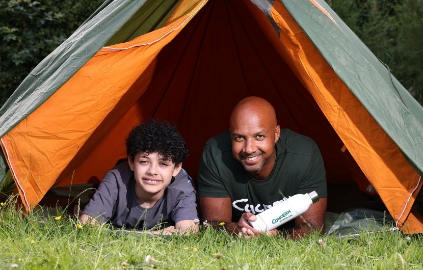 Two people, a man and an older child, in a tent outside looking straight ahead