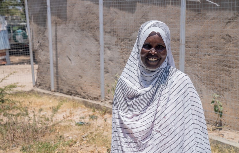 Woman smiling, stand outside wearing a white and grey striped head scarf