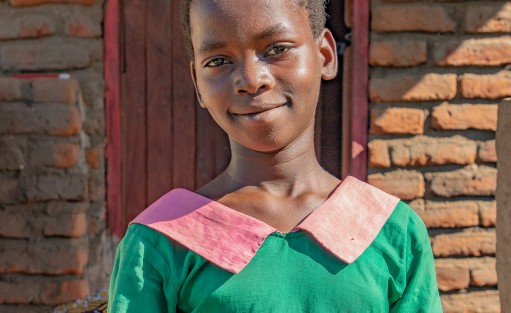 A girl dressed in her school uniform stands in front of her family's home