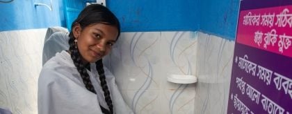 A young girl washes her hands and smiles