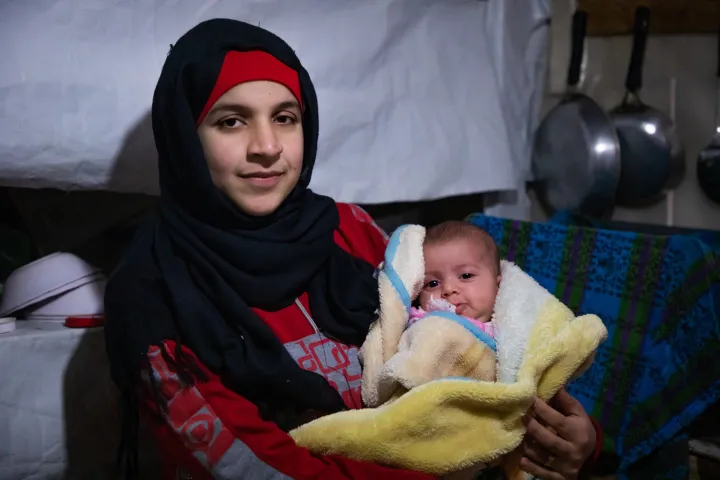 Wafdeh* (20) with her youngest daughter Rajaa* (2 months) with their thermal blanket in their makeshift kitchen. Photo: Gavin Douglas / Concern Worldwide. Wafdeh* (20) with her youngest daughter Rajaa* (2 months) with their thermal blanket in their makeshift kitchen. Photo: Gavin Douglas / Concern Worldwide.