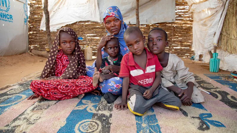 Hamila and her four children sitting on ground of tent in refugee camp in Chad