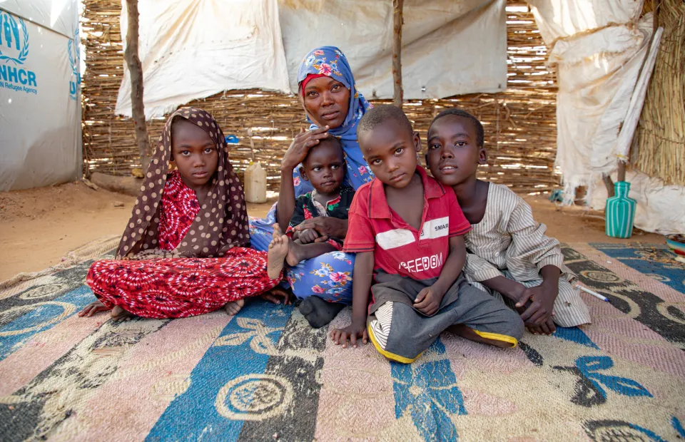 Hamila and her four children sitting on ground of tent in refugee camp in Chad
