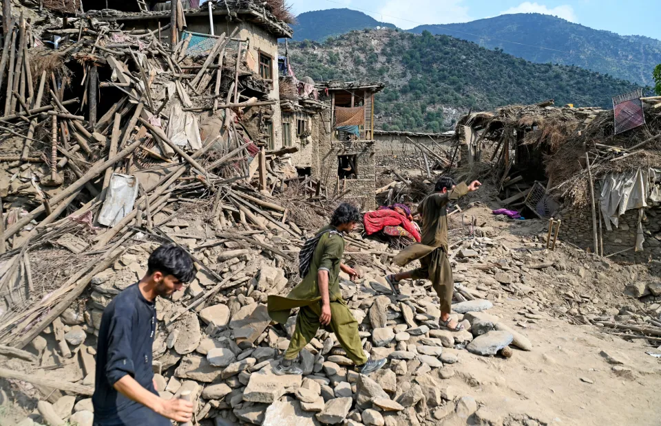 Afghans walk past houses damaged by earthquakes in Kunar province, in Eastern Afghanistan, on September 1, 2025