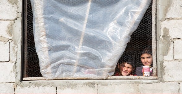 Syrian refugee Afaf, 8, and her younger brother Hani, 4, stand by the window of the kitchen in the collective shelter where they live with their family in Akroum, in Akkar, north Lebanon. Photo: Dalia Khamissy / Concern Worldwide.