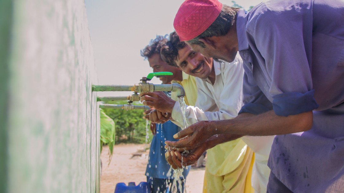 Two local men, Naaju and Rajesh are talking to each other happily while drinking water from water plant installed by Concern Worldwide. Photo: Black Box Sounds/ Concern Worldwide.