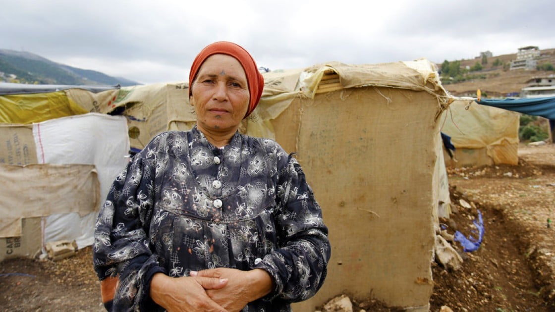 A 55-year old Syrian refugee stands in front of her makeshift shelter in an informal tented settlement near the Syrian border in north Lebanon, February 2015. Photo taken by Dalia Khamissy / Concern Worldwide.