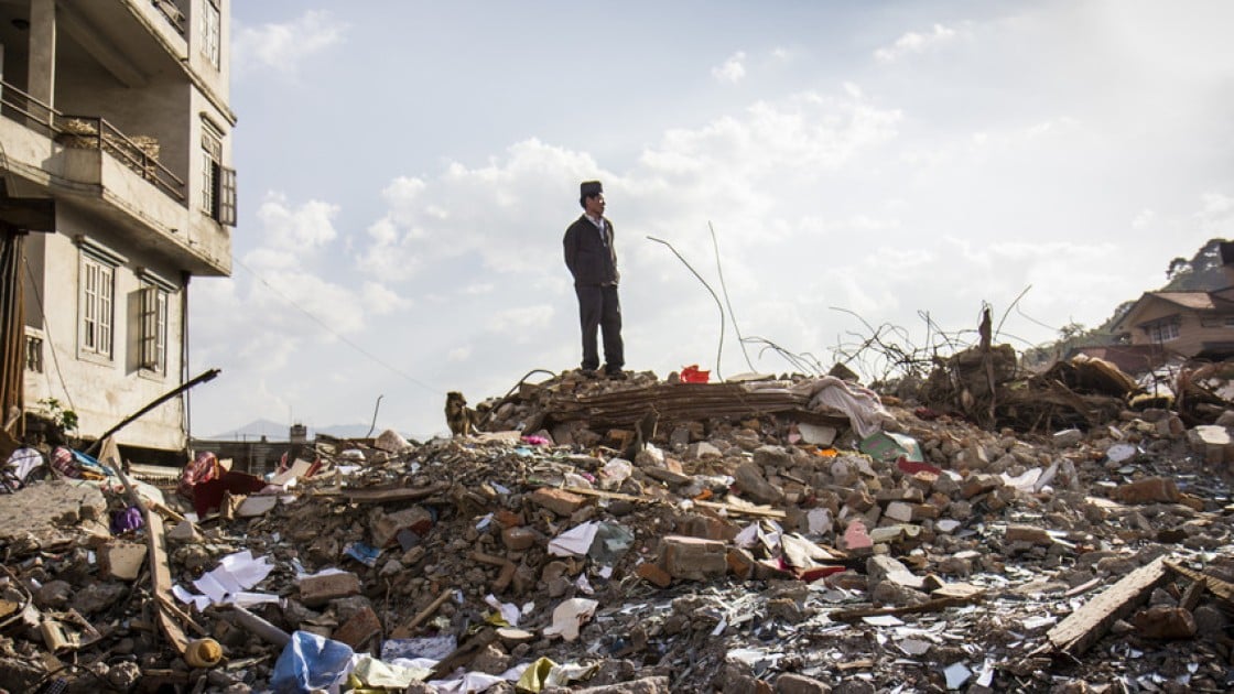 a man standing on the rubble of a building left by the Nepal earthquake. Photo: Helvetas.