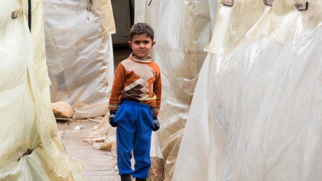 A young Syrian refugee stands between the tents at an informal settlement in the north of Lebanon. Photo: Dalia Khamissy / Concern Worldwide.