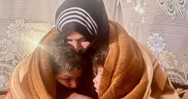 A woman and two boys huddle together with a warm blanket wrapped around themselves