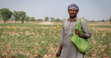 Farmer Maula stands in field in Pakistan with green bag of seeds