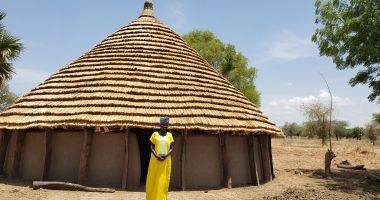 Abuk Wieu in front of her tukul house constructed using savings from the Village Savings and Loans Association.