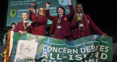 Four team members from Laurel Hill Secondary school stand on a stage with a banner in front of them, after receiving their awards for winning the Concern 2025 Debate final