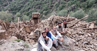 Four men sitting next to a completely collapsed building in Kunar Valley, Afghanistan