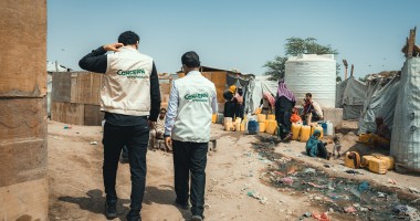 Concern’s health staff and the Country Director Victor Moses visit a displacement camp in Yemen, with people filling a water tank in the background