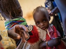 Baby looking at camera, being held by woman wearing beaded necklaces