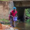 Woman collects water in bright plastic bucket.